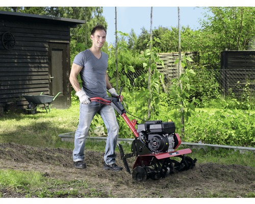 Muž pracuje s rotačním kultivátorem na zahradě pro zpracování půdy.