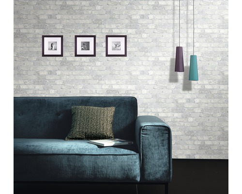 Obývací pokoj s pohovkou, polštářem, obrazy a závěsnými svítidly před zděnou stěnou se vzorem