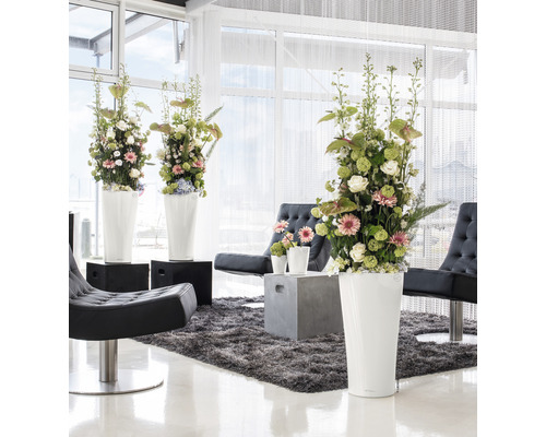 Světlý interiér s květinovou výzdobou ve vysokých květináčích, křeslech a koberci