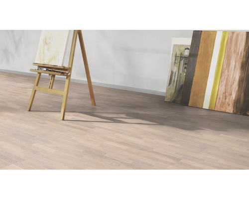 Pohled do místnosti se světlou laminátovou podlahou, malířským stojanem a obrazy