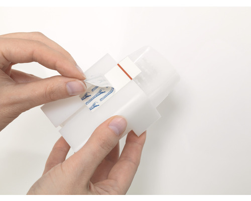 Osoba odstraňuje ochrannou fólii z upevňovacího proužku na zařízení.