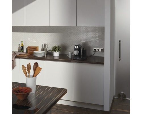 Světlá kuchyně s pracovní deskou, kuchyňským náčiním, kávovarem a obkládanou zadní stěnou