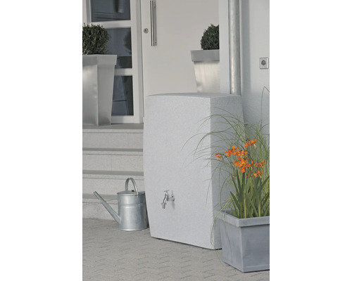 Nádrž na vodu s kohoutkem, konví a rostlinami před domem