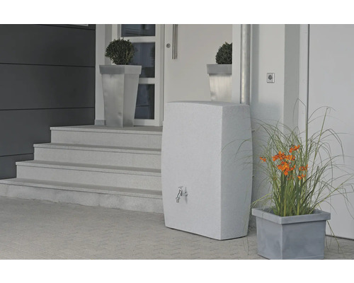 Snímek fasády domu se stylovým zásobníkem vody s kohoutkem, po stranách jsou květináče s rostlinami