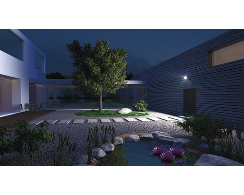 Osvětlená zahrada s rybníkem, kameny, rostlinami a moderním domem v noci.