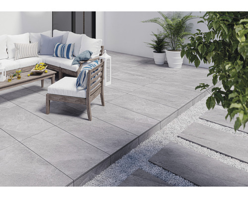 Terasa se šedými dlaždicemi, zahradním nábytkem a rostlinami.