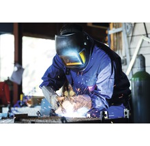 Svářeč se svářečskou helmou a rukavicemi pracuje s kovem.