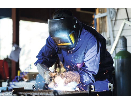 Svářeč se svářečskou helmou a rukavicemi pracuje s kovem.