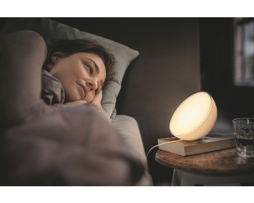 Žena leží v posteli vedle noční lampy.