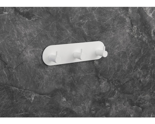 Bílá nástěnná věšáková stěna se třemi háčky na šedé mramorové stěně.