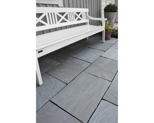 Zahradní prostor s šedými terasovými deskami a bílou zahradní lavicí