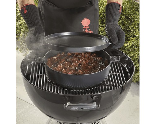 Osoba připravuje pokrm v litinovém hrnci na grilu.