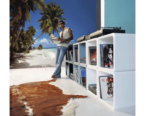 Obývací pokoj s bílými regály, gramofonem a osobou s deskou před tapetou s plážovou tématikou