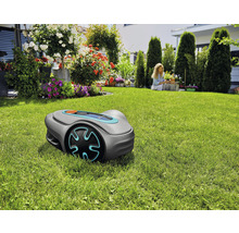 Robotická sekačka na trávníku v zahradě s květinami a ženou