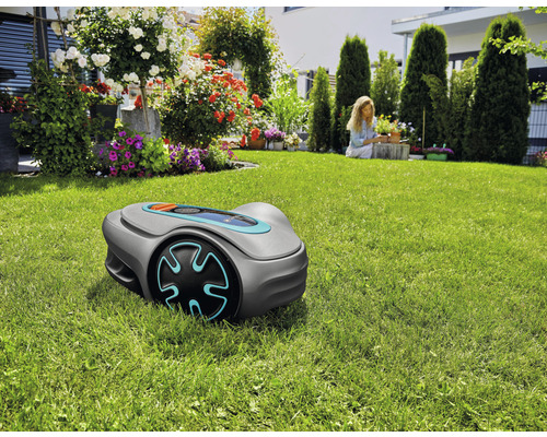 Robotická sekačka na trávníku v zahradě s květinami a ženou