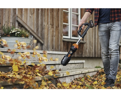 Osoba odstraňuje listí z schodů před domem pomocí akumulátorového foukače listí.