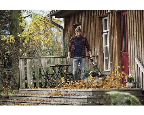 Muž používá foukač listí na dřevěné terase domu