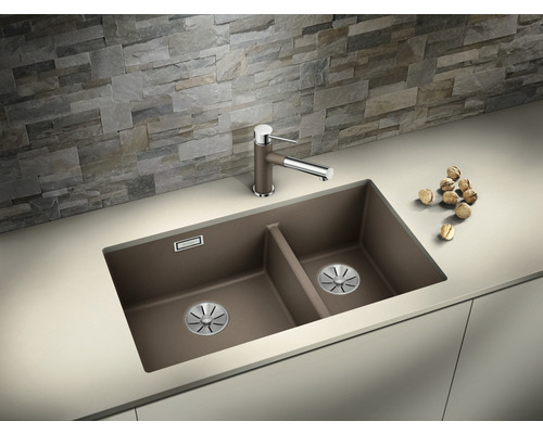 Dvojitý dřez s baterií na kuchyňské lince před kamennou zdí