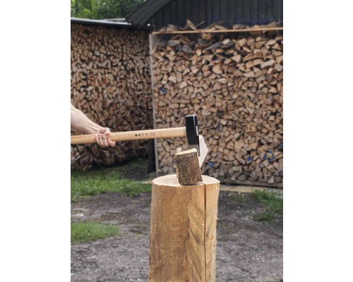 Sekání dřeva sekerou na špalku před hromadou dřeva