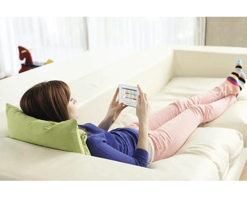 Žena ovládá topení pomocí tabletu chytré domácnosti na pohovce