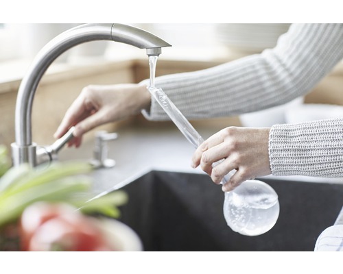 Žena plní skleněnou láhev vodou z kohoutku