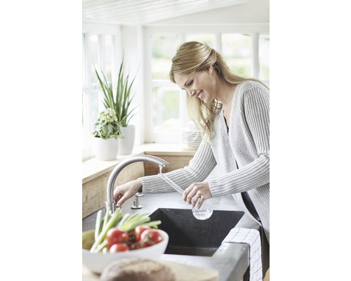 Žena myje zeleninu v kuchyňském dřezu s baterií.