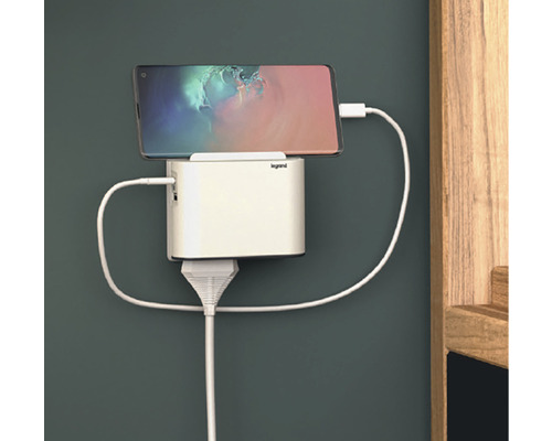 Mobilní telefon připojený k bílé nabíjecí stanici na zdi