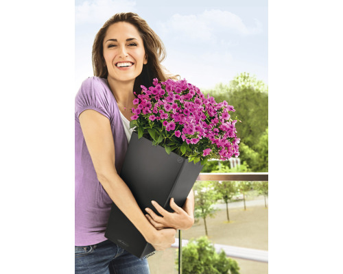 Žena drží černý květináč s fialovými květinami na balkoně
