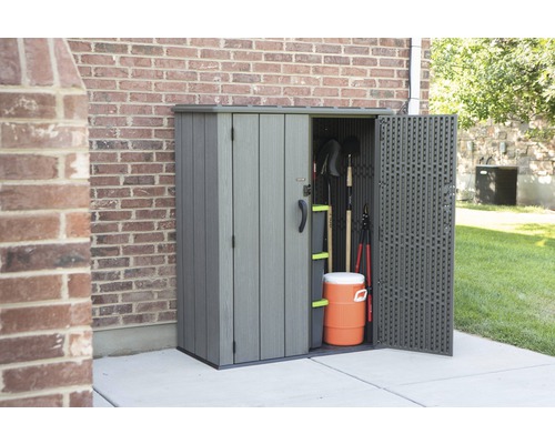 Zahradní skříň s otevřenými dveřmi vedle cihlové budovy, plná zahradního nářadí a nádoby na nápoje.