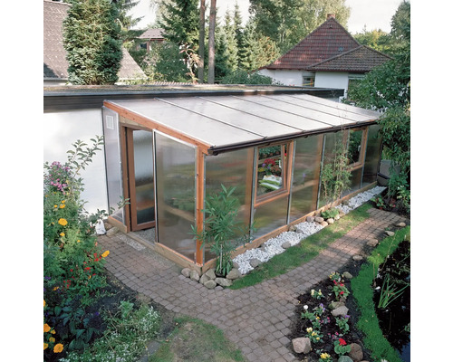 Skleník s dřevěnými prvky a průhlednými stěnami na zahradě.