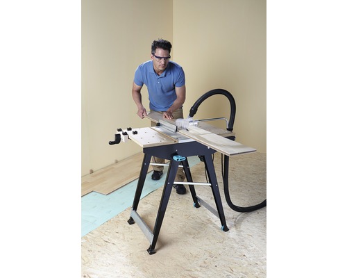 Muž pracuje se stolní pilou na pracovním stole a má ochranné brýle.