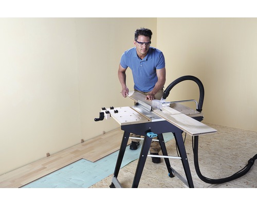 Muž řeže dřevěnou desku stolní pilou ve světlé místnosti