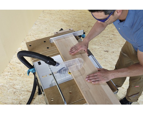 Muž řeže dřevěnou desku kotoučovou pilou na pracovním stole