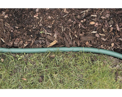 Detailní záběr mulčovací kůry, trávníku a zelené zahradní hadice jako oddělovače