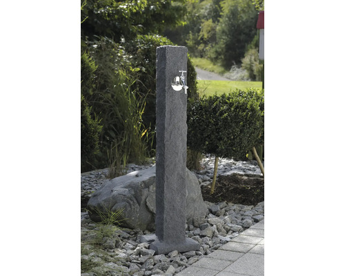 Zahradní scéna s kamenným vodním sloupkem s kovovým kohoutkem.