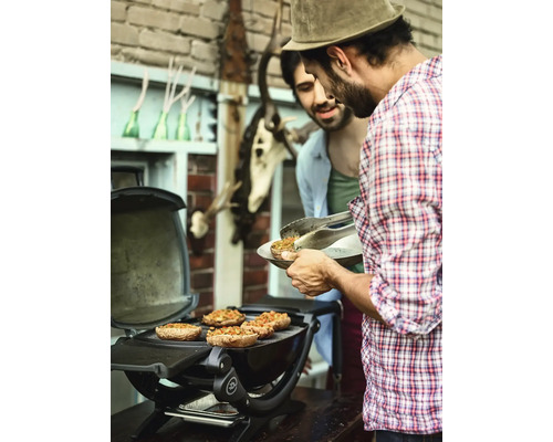 Dva muži grilují plněné žampiony na kulatém grilu venku.