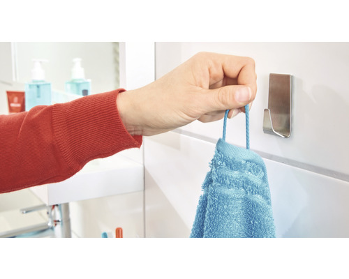 Ruka věší modrý ručník na háček na ručníky v koupelně