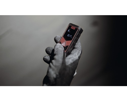 Ruka s pracovní rukavicí drží laserový dálkoměr.