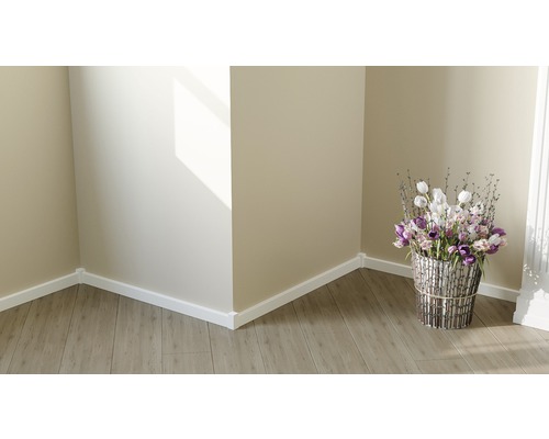 Pohled do místnosti s dřevěnou podlahou, bílými podlahovými lištami a květinovou vazbou ve stříbrném květináči