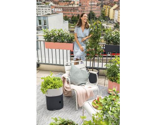 Balkónová scéna s ženou, židlí, květináči a výhledem na město