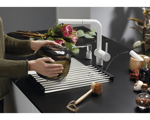 Žena myje skleněnou vázu v dřezu s odkapávačem a vodovodní baterií