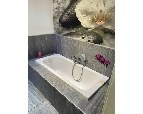 Koupelna se zabudovanou vanou, šedými obklady a květinovým vzorem na zdi