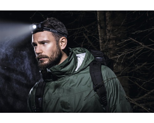 Muž s čelovkou Varta a batohem venku