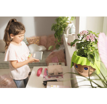 Dívka s poznámkovým blokem vedle květináče s designem obličeje v dětském pokoji.