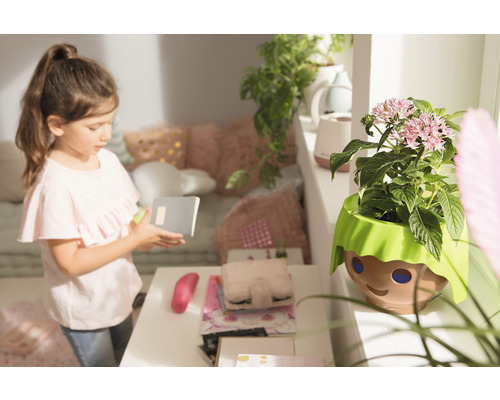 Dívka s poznámkovým blokem vedle květináče s designem obličeje v dětském pokoji.