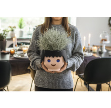 Žena drží květináč ve tvaru stylizované hlavy s rostlinou