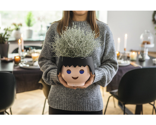 Žena drží květináč ve tvaru stylizované hlavy s rostlinou