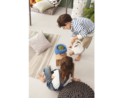 Dvě děti v interiéru, jedno zalévá rostlinu v květináči s obličejem konví.