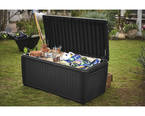 Otevřená černá zahradní truhla plná zahradního náčiní na zahradě