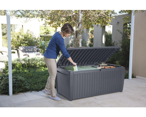 Žena otevírá venkovní úložný box odolný proti povětrnostním vlivům pro polštáře a zahradní nářadí